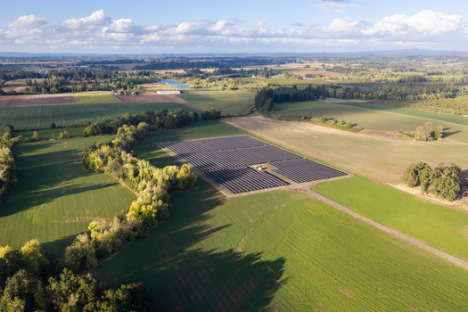 Aerial view of a solar farm situated in a rural landscape with green fields trees and a clear blue sky in Woodburn Oregon United States. Aerial view of a solar farm situated in a rural landscape with green fields trees and a clear blue sky in Woodburn Oregon United States.