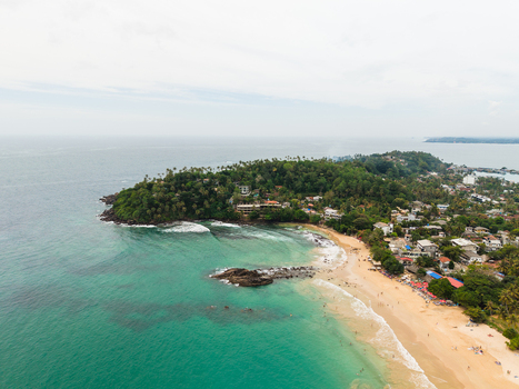 Aerial view of the tropical coastline of Mirissa Beach featuring Parrot Rock turquoise waters and lush palm trees in Mirissa Southern Province Sri Lanka. Aerial view of the tropical coastline of Mirissa Beach featuring Parrot Rock turquoise waters and lush palm trees in Mirissa Southern Province Sri Lanka.