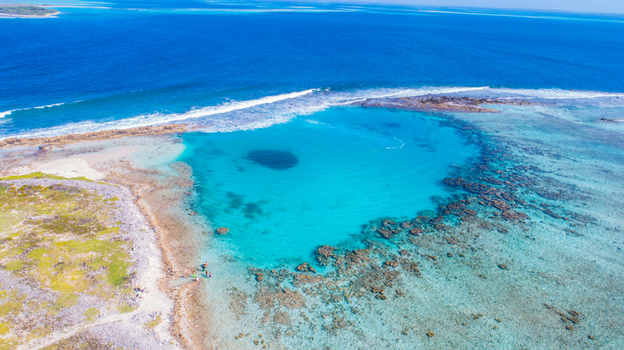 Aerial view of Los Roques archipelago featuring a vibrant turquoise lagoon coral reefs and clear shallow water with people on the sandy shore in Los Roques Dependencias Federales Venezuela. Aerial view of Los Roques archipelago featuring a vibrant turquoise lagoon coral reefs and clear shallow water with people on the sandy shore in Los Roques Dependencias Federales Venezuela.