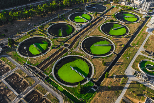 Aerial view of the water treatment plant featuring large circular sedimentation tanks with green water and industrial infrastructure surrounded by trees in Rome Lazio Italy.