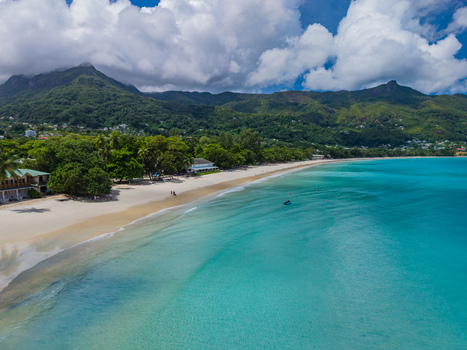 Aerial view of the pristine white beach meeting the turquoise waters backed by lush green mountains under a partly cloudy sky Victoria Seychelles. Aerial view of the pristine white beach meeting the turquoise waters backed by lush green mountains under a partly cloudy sky Victoria Seychelles.