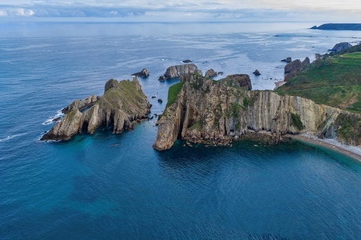 Aerial view of Silence Beach Viewpoint featuring dramatic jagged rock formations turquoise water and lush green coastal hills in Cudillero Asturias Spain.