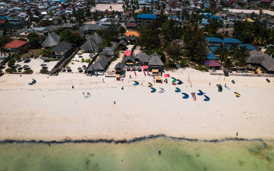Aerial view of the sun kissed beach dotted with colorful kites and thatched roof structures where the turquoise waters meet the pristine sands Paje Unguja South Region Tanzania. Aerial view of the sun kissed beach dotted with colorful kites and thatched roof structures where the turquoise waters meet the pristine sands Paje Unguja South Region Tanzania.