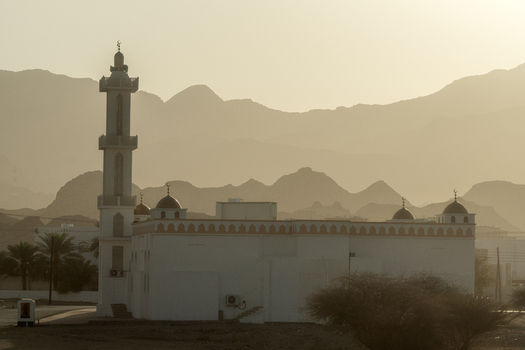 View of a mosque with a tall minaret set against a backdrop of hazy mountains during golden hour in Muscat Muscat Governorate Oman. View of a mosque with a tall minaret set against a backdrop of hazy mountains during golden hour in Muscat Muscat Governorate Oman.
