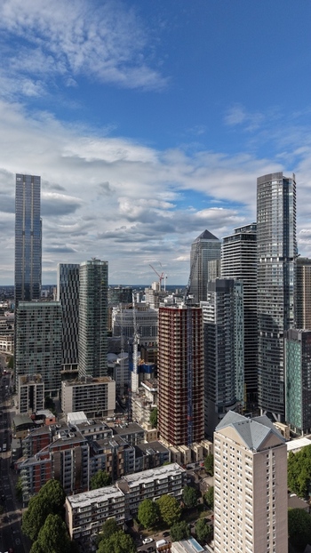 London United Kingdom 16 June 2026 Aerial view of Canary Wharf financial district featuring modern skyscrapers and construction cranes under a blue sky with scattered clouds.