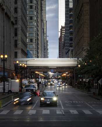 Chicago United States 15 September 2025 View of a busy city street at dusk with an elevated CTA train passing over the road and cars with headlights on.