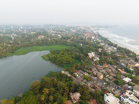 Aerial view of the lush tropical landscape and residential rooftops between a calm lake and the ocean waves in Galle Southern Province Sri Lanka.