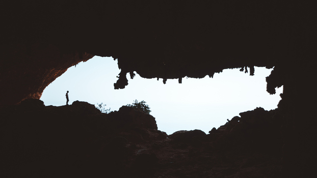 View of a person standing in the silhouette of the large entrance of Hoq Cave with rugged rock formations and a bright sky visible in the background in Socotra Socotra Yemen. View of a person standing in the silhouette of the large entrance of Hoq Cave with rugged rock formations and a bright sky visible in the background in Socotra Socotra Yemen.
