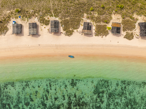 Aerial view of Pink Beach with small wooden huts along the sandy shore and a boat in the turquoise water of East Nusa Tenggara Indonesia. Aerial view of Pink Beach with small wooden huts along the sandy shore and a boat in the turquoise water of East Nusa Tenggara Indonesia.