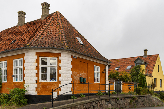 View of a historic orange house with a red tiled roof white corner quoins and a black iron railing in Praesto Seeland Denmark. View of a historic orange house with a red tiled roof white corner quoins and a black iron railing in Praesto Seeland Denmark.