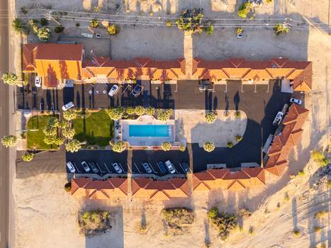 Twentynine Palms United States 07 April 2026 Aerial view of El Rancho Dolores Motel featuring a central swimming pool palm trees and parked cars in the desert landscape.