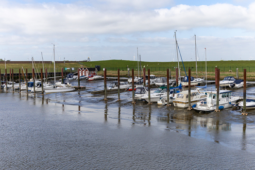 View of Dangast harbor with boats resting on the mud during low tide wooden pilings and a green dike under a cloudy sky in Varel Lower Saxony Germany. View of Dangast harbor with boats resting on the mud during low tide wooden pilings and a green dike under a cloudy sky in Varel Lower Saxony Germany.