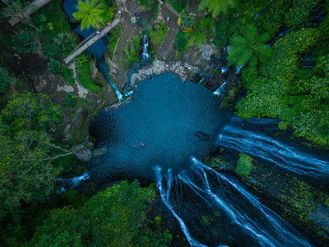 Aerial view of Banyumala Waterfall with its cascading water flowing into a deep blue pool surrounded by lush tropical forest and greenery in Sukasada Bali Indonesia.