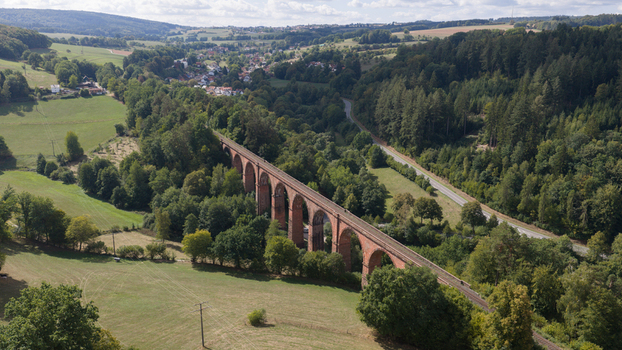 Aerial view of the historic Himbaechel Viadukt red sandstone railway bridge surrounded by lush green forests and rolling hills in Erbach Hessen Germany.