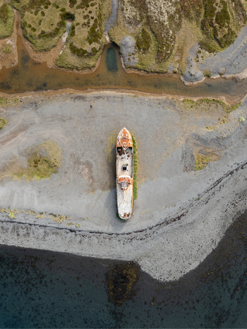 Aerial view of a decaying ship resting on the shore embraced by the contrasting textures of sand water and earth Westfjords Iceland. Aerial view of a decaying ship resting on the shore embraced by the contrasting textures of sand water and earth Westfjords Iceland.
