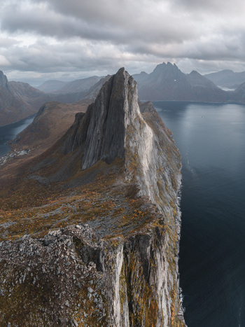 Aerial view of the dramatic Segla mountain peak rising sharply above the deep blue waters of the fjord in Senja Troms Norway.