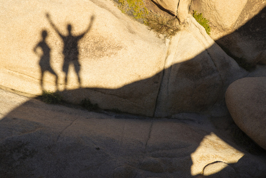 View of the shadows of two people cast on a large textured rock formation in Joshua Tree California United States.