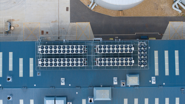 Aerial view of the Fenland Glasshouse Energy Centre showing industrial cooling fans on a blue corrugated roof and a large storage tank in Chittering England United Kingdom.