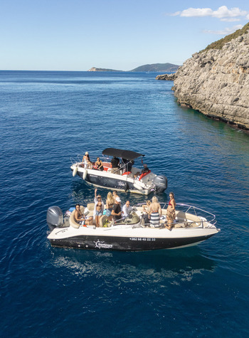 Aerial view of two motorboats filled with people enjoying a sunny day in the clear blue waters of the Adriatic Sea near the rocky coastline of Tivat Tivat Municipality Montenegro. Aerial view of two motorboats filled with people enjoying a sunny day in the clear blue waters of the Adriatic Sea near the rocky coastline of Tivat Tivat Municipality Montenegro.