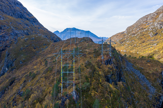 Aerial view of high voltage power lines stretching across a rugged mountainous landscape with autumn foliage and a distant lake Andalsnes More og Romsdal Norway. Aerial view of high voltage power lines stretching across a rugged mountainous landscape with autumn foliage and a distant lake Andalsnes More og Romsdal Norway.