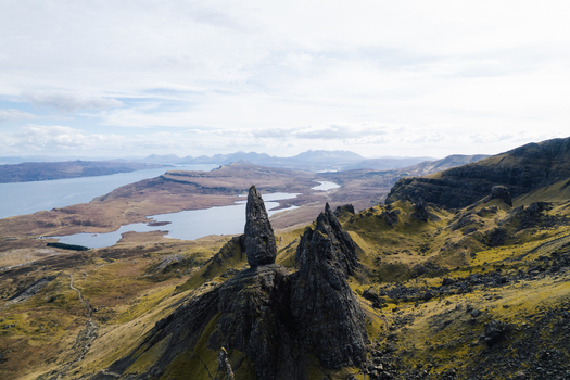 Aerial view of The Storr rock formation rising above the rugged grassy slopes and distant lochs of the Isle of Skye in Portree Scotland United Kingdom. Aerial view of The Storr rock formation rising above the rugged grassy slopes and distant lochs of the Isle of Skye in Portree Scotland United Kingdom.