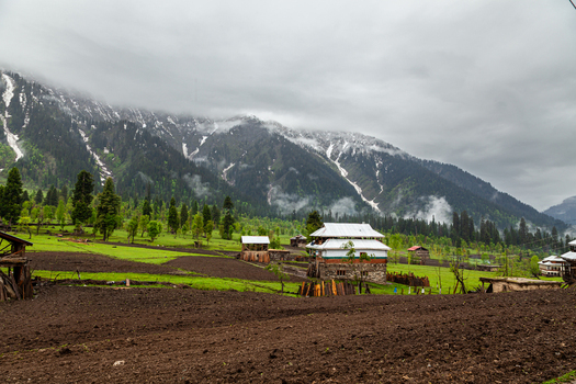View of traditional wooden houses and cultivated fields in the lush green meadows of Arang Kel village with snow capped mountains under a cloudy sky Arang Kel Azad Kashmir Pakistan. View of traditional wooden houses and cultivated fields in the lush green meadows of Arang Kel village with snow capped mountains under a cloudy sky Arang Kel Azad Kashmir Pakistan.
