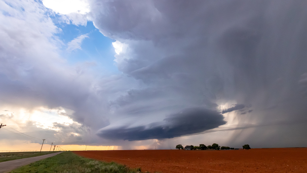 View of a dramatic supercell storm cloud hovering over a vast red dirt field in rural Oklahoma City Oklahoma United States.