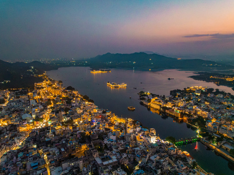 Aerial view of Lake Pichola at twilight with illuminated buildings and the City Palace reflecting on the water in Udaipur Rajasthan India.