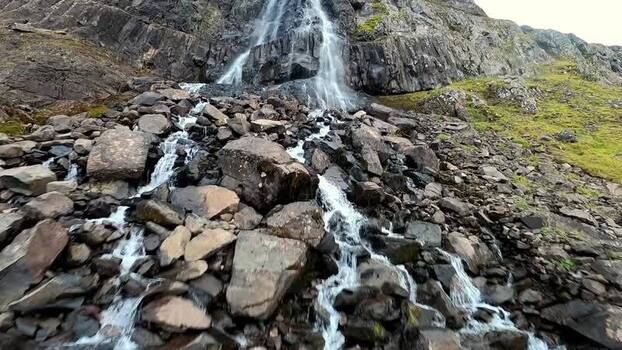 FPV aerial view of waterfall over rocky terrain Iceland.
