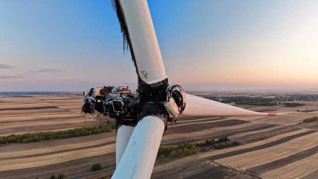 Aerial view of a damaged wind turbine with charred blades and nacelle set against a vast agricultural landscape during golden hour in Vladimirovac Vojvodina Serbia.