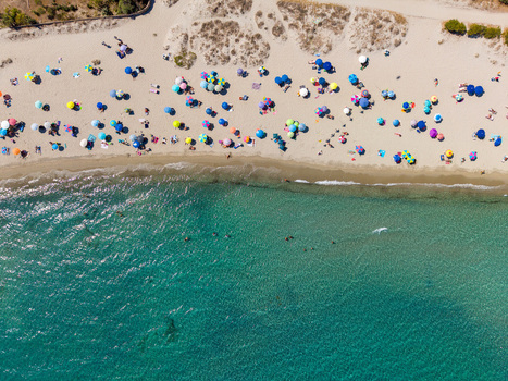 Aerial view of Pittulongu beach with colorful umbrellas scattered across the sand and people swimming in the turquoise water of the Mediterranean Sea in Pittulongu Sardinia Italy.