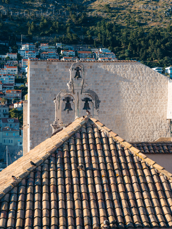 View of terracotta tiled rooftops and a stone bell tower with three bells against a hillside background in Dubrovnik Dubrovnik Neretva County Croatia. View of terracotta tiled rooftops and a stone bell tower with three bells against a hillside background in Dubrovnik Dubrovnik Neretva County Croatia.