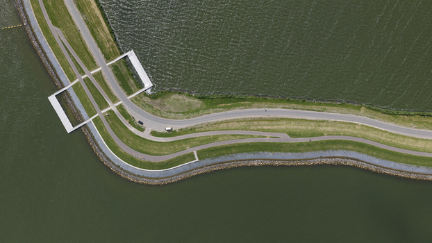 Aerial view of a dike road winding along the water with a small bridge structure and green grass in Uitdam North Holland Netherlands.