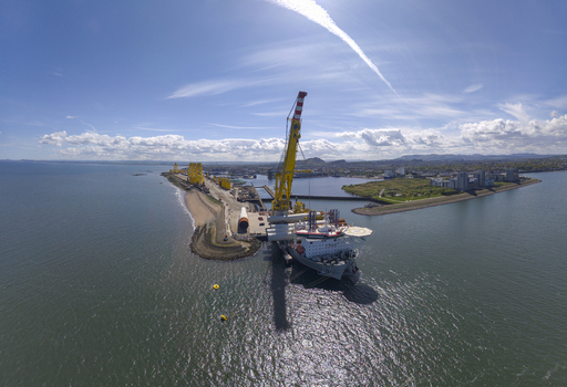 Aerial view of the industrial port of Leith featuring a large yellow crane and a docked ship under a clear blue sky in Edinburgh Scotland United Kingdom. Aerial view of the industrial port of Leith featuring a large yellow crane and a docked ship under a clear blue sky in Edinburgh Scotland United Kingdom.