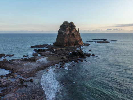 Aerial view of Papuma Beach with its iconic large rock formation rising from the sea surrounded by rocky shoreline and gentle waves in Jember East Java Indonesia. Aerial view of Papuma Beach with its iconic large rock formation rising from the sea surrounded by rocky shoreline and gentle waves in Jember East Java Indonesia.
