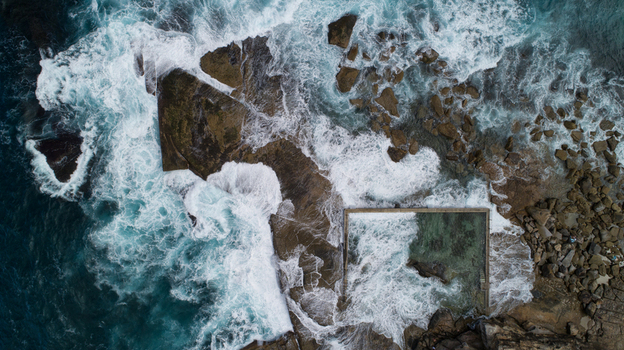 Aerial view of Newport Rock Pool with crashing waves white foam and turquoise water against rugged coastal rocks in Sydney New South Wales Australia.