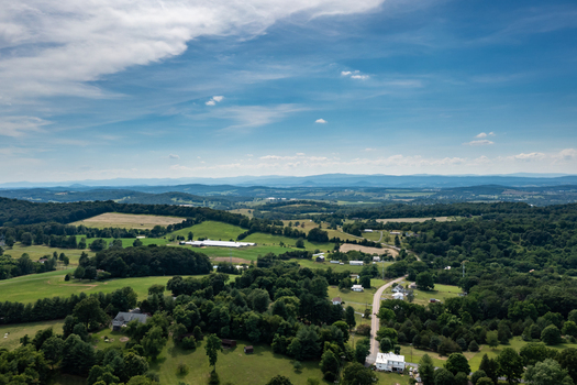 Harrisonburg Virginia United States 09 August 2021 Aerial view of rolling green hills farmland and scattered houses under a bright blue sky in the Shenandoah Valley. Harrisonburg Virginia United States 09 August 2021 Aerial view of rolling green hills farmland and scattered houses under a bright blue sky in the Shenandoah Valley.
