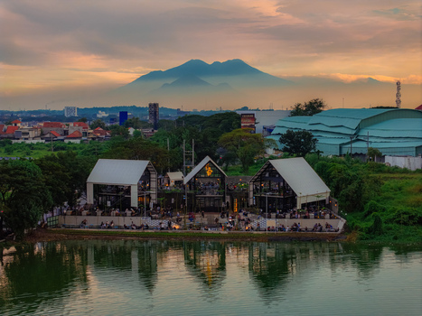 Aerial view of Unesa Lake with modern buildings A frame roofs lush greenery and a distant mountain silhouette under a sunset sky in Kecamatan Lakarsantri Jawa Timur Indonesia. Aerial view of Unesa Lake with modern buildings A frame roofs lush greenery and a distant mountain silhouette under a sunset sky in Kecamatan Lakarsantri Jawa Timur Indonesia.