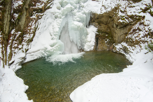 Aerial view of Casoca Pruncea Waterfall surrounded by snow covered rocks and ice formations with a clear pool of water in Casoca Buzau County Romania.
