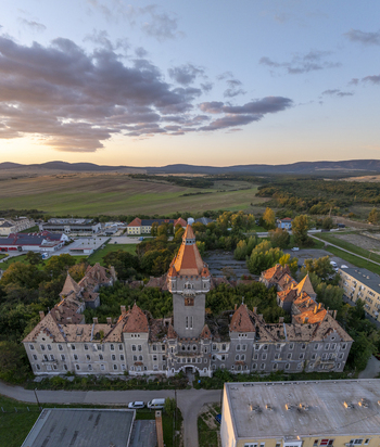 Aerial view of the historic Hajmasker Barracks with its central tower and overgrown courtyard surrounded by rural fields and trees under a golden sunset sky in Hajmasker Hungary. Aerial view of the historic Hajmasker Barracks with its central tower and overgrown courtyard surrounded by rural fields and trees under a golden sunset sky in Hajmasker Hungary.