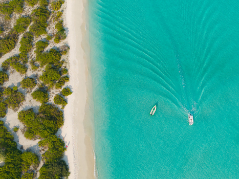 Aerial view of turquoise waters meeting pristine white sands along the coast with boats gently cruising Dhidhdhoo Thiladhunmathi Atoll Maldives.
