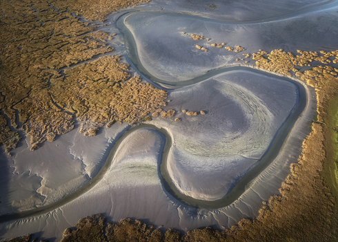 Aerial view of the Rogerstown Estuary featuring winding water channels textured mudflats and golden salt marshes at sunset in Lusk County Dublin Ireland. Aerial view of the Rogerstown Estuary featuring winding water channels textured mudflats and golden salt marshes at sunset in Lusk County Dublin Ireland.