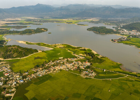 Aerial view of Lak Lake surrounded by vibrant green rice paddies and a small village with mountains in the distance in Lien Son Lak Dak Lak Vietnam. Aerial view of Lak Lake surrounded by vibrant green rice paddies and a small village with mountains in the distance in Lien Son Lak Dak Lak Vietnam.