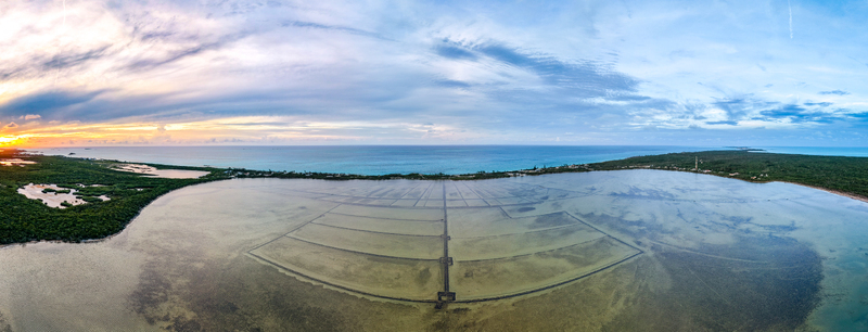 Aerial view of the geometric patterns of Salt Pond surrounded by lush green vegetation and the turquoise ocean under a dramatic sunset sky Exuma Exuma The Bahamas.