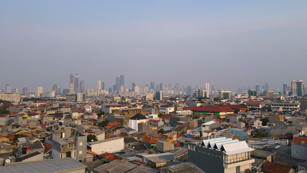 Aerial view of the dense urban landscape and skyline of Jakarta featuring numerous rooftops residential buildings and modern skyscrapers in West Jakarta Jakarta Indonesia.