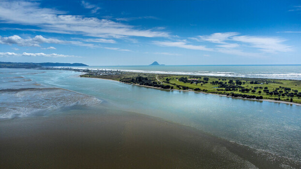 Aerial view of the coastal spit at Ohope Beach with lush green parkland sandy shores and the Pacific Ocean under a bright blue sky in Ohope Bay of Plenty Region New Zealand.