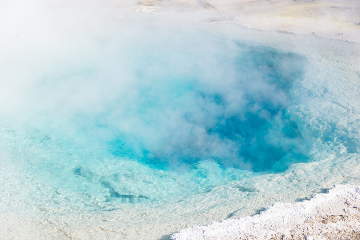 View of a vibrant blue geothermal hot spring with steam rising from the mineral rich water in Yellowstone National Park United States.