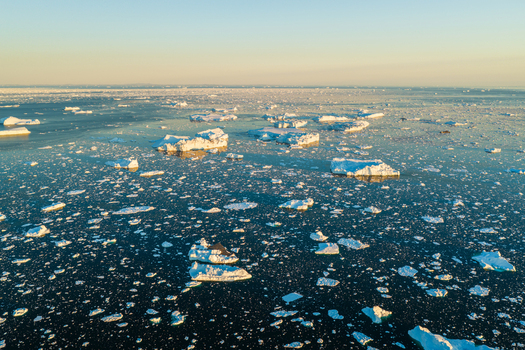 Aerial view of icebergs floating in the dark blue waters of the Ilulissat Icefjord under the soft golden light of the arctic sun Ilulissat Avannaata Municipalit Greenland.