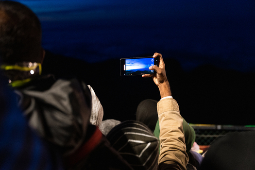 View of a person taking a photo with a smartphone of the sunrise from Adam s Peak surrounded by a crowd of pilgrims in Ratnapura Sabaragamuwa Province Sri Lanka. View of a person taking a photo with a smartphone of the sunrise from Adam s Peak surrounded by a crowd of pilgrims in Ratnapura Sabaragamuwa Province Sri Lanka.