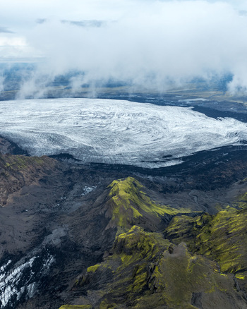 Aerial view of the expansive Myrdalsjokull glacier surrounded by moss covered volcanic ridges and dramatic clouds in Vik Myrdalshreppur Iceland.